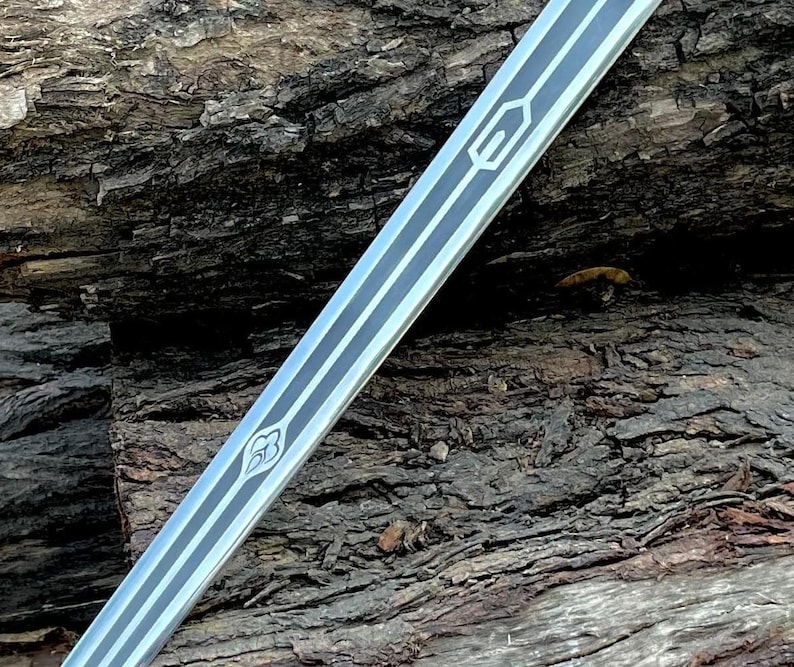 May include: A silver sword blade with black and white decorative lines and geometric designs. The blade is angled across a textured, brown wooden surface. The sword's design features a series of parallel lines and stylized symbols.