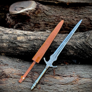 May include: A silver and bronze sword with an ornate handle and a leather sheath. The sword's blade has a pointed tip and a decorative design. The sheath is brown and has a strap with a buckle. The sword is approximately 28 inches long.
