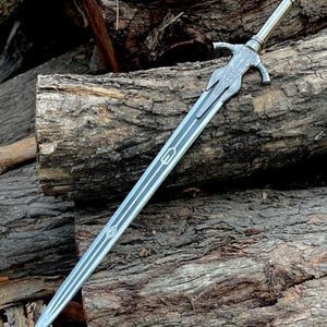 May include: A silver sword with a detailed hilt and blade design. The blade has a central groove with two parallel lines. The sword rests on a pile of rough-hewn logs, showcasing its craftsmanship and medieval aesthetic.