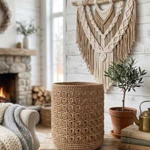 May include: A cylindrical woven basket with a textured, repeating open-stitch pattern in a natural tan colour. The basket features a sturdy, flat base and a consistent, open-weave construction throughout its body, showcasing a uniform, earthy tone.