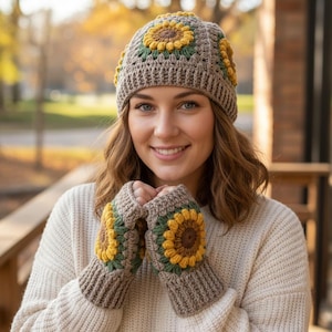 May include: A crocheted hat and fingerless gloves set. The hat and gloves are brown with yellow, green, and brown sunflower designs. The hat has a ribbed brim and the gloves have a ribbed cuff. The background is blurred, with fall foliage.