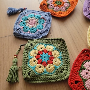 May include: Five crocheted squares with colorful floral designs. Each square has a different color scheme, including green, blue, orange, red, and purple.