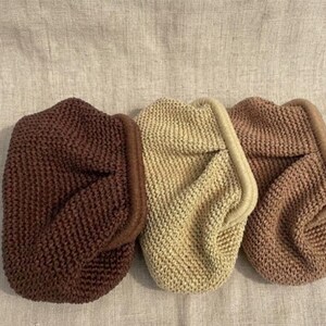 May include: Three knitted pouches in shades of brown, beige, and rose. Each pouch has a folded flap and a contrasting trim. The pouches are made of a textured knit material.