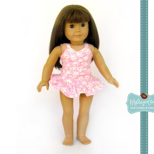May include: A doll wearing a pink swimsuit with a white daisy pattern. The swimsuit has a ruffled skirt. The doll has brown hair and is standing against a white background. The image includes the text "MyAngieGirl Doll Clothes & Patterns".