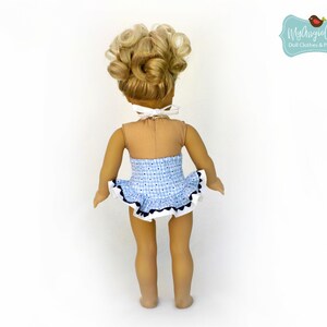 Puede incluir: Una mu&ntilde;eca con un traje de ba&ntilde;o de cuadros azules y blancos con una falda con volantes y ribete negro. La mu&ntilde;eca tiene el pelo rubio rizado y un lazo blanco alrededor del cuello. El tono de piel de la mu&ntilde;eca es bronceado.