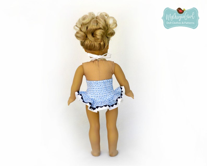 Puede incluir: Una mu&ntilde;eca con un traje de ba&ntilde;o de cuadros azules y blancos con una falda con volantes y ribete negro. La mu&ntilde;eca tiene el pelo rubio rizado y un lazo blanco alrededor del cuello. El tono de piel de la mu&ntilde;eca es bronceado.