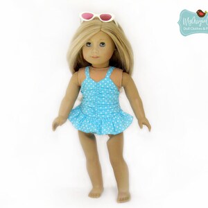 May include: A doll wearing a light blue swimsuit with white polka dots and a ruffled skirt. The doll has blonde hair and is wearing white sunglasses on top of its head. The image includes the text "MyAngieGirl Doll Clothes & Patterns."