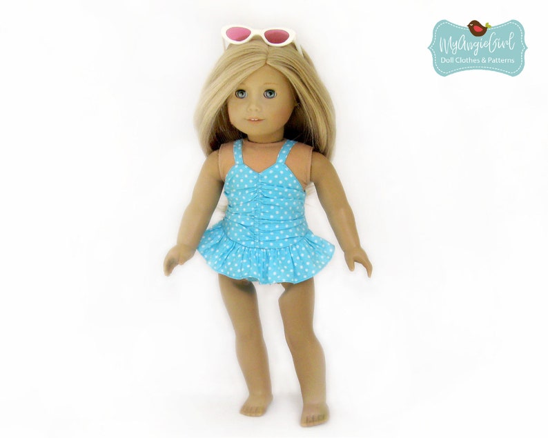 May include: A doll wearing a light blue swimsuit with white polka dots and a ruffled skirt. The doll has blonde hair and is wearing white sunglasses on top of its head. The image includes the text "MyAngieGirl Doll Clothes & Patterns."