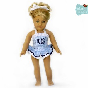 Puede incluir: Una mu&ntilde;eca con un traje de ba&ntilde;o de cuadros azules y blancos con una falda con volantes y un monograma. El traje de ba&ntilde;o tiene tirantes y ribetes blancos, y un borde azul marino. La mu&ntilde;eca tiene el pelo rubio y un lazo blanco.