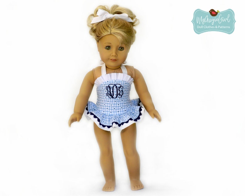 Puede incluir: Una mu&ntilde;eca con un traje de ba&ntilde;o de cuadros azules y blancos con una falda con volantes y un monograma. El traje de ba&ntilde;o tiene tirantes y ribetes blancos, y un borde azul marino. La mu&ntilde;eca tiene el pelo rubio y un lazo blanco.