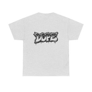 May include: Light grey t-shirt with a black and white graffiti-style design that reads "DOPE". The word is stylized with dripping paint effects, adding a street art aesthetic to the casual wear.