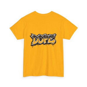 May include: Mustard yellow t-shirt featuring the word "DOPE" in a graffiti-style design. The word is outlined in black with a white fill and dripping paint effect. The shirt is a short-sleeved crew neck.
