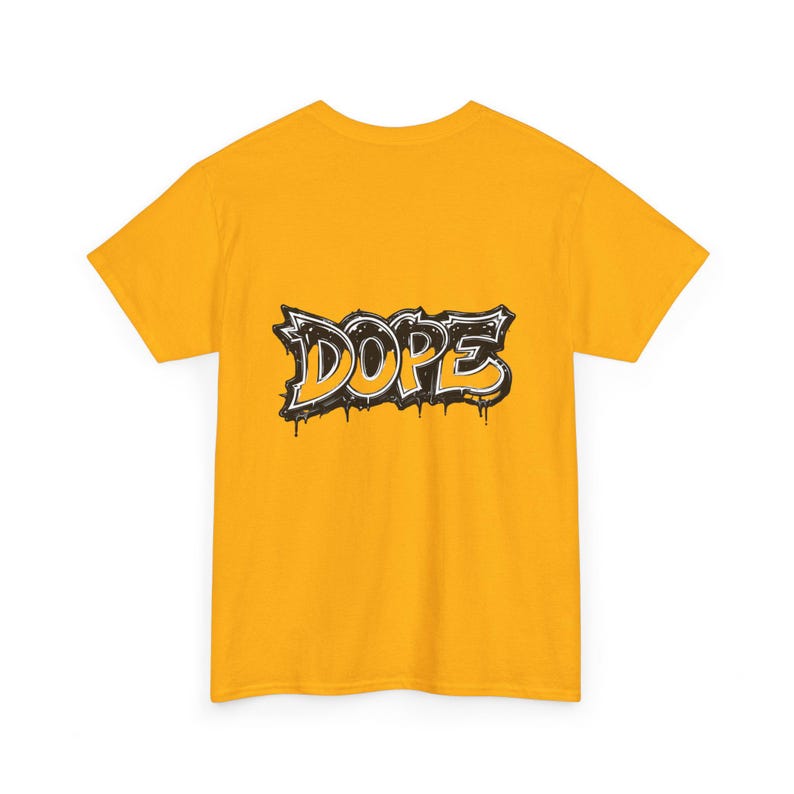 May include: Mustard yellow t-shirt featuring the word "DOPE" in a graffiti-style design. The word is outlined in black with a white fill and dripping paint effect. The shirt is a short-sleeved crew neck.