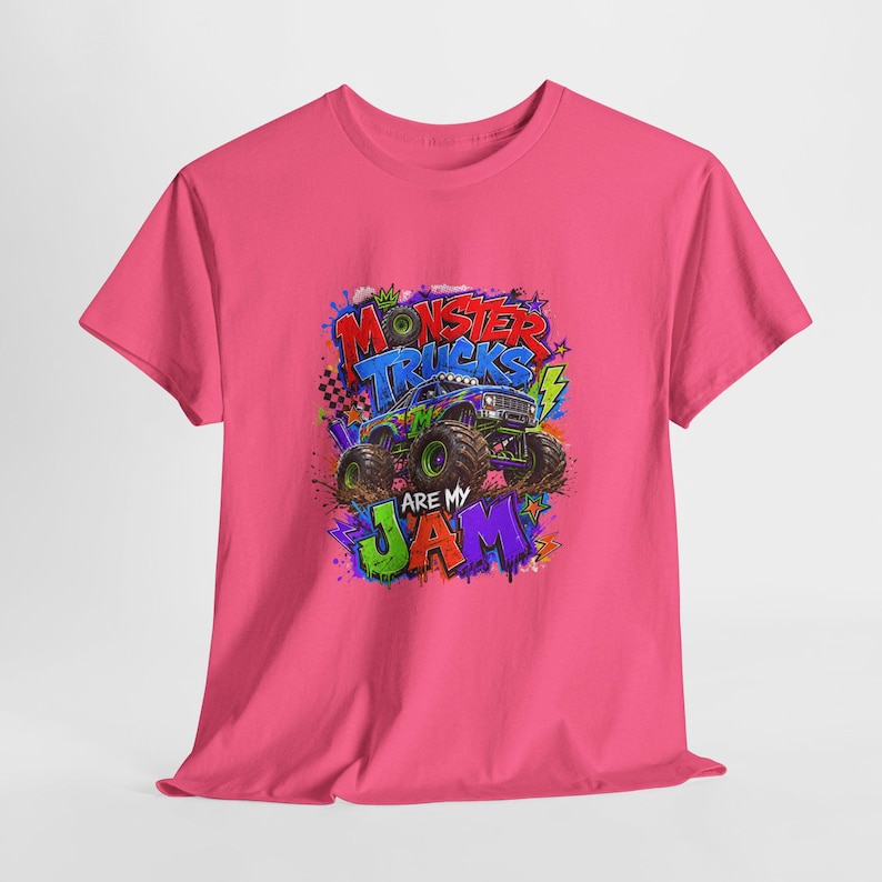 Może przedstawiać: R&oacute;żowa koszulka z kolorową grafiką monster trucka i napisem "Monster Trucks Are My Jam". Projekt zawiera koronę, błyskawice i elementy w stylu graffiti, tworząc żywy i zabawny wygląd.