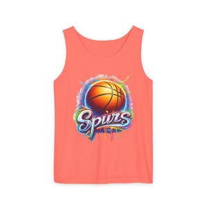 May include: Coral-colored tank top featuring a basketball graphic with the word "Spurs" in a stylized font. The basketball is orange with black lines, set against a colorful, splash-like background. A sporty apparel item.