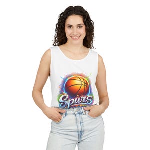 May include: White tank top featuring a basketball graphic with the word "Spurs" in a colorful design. The basketball is orange with black lines, set against a vibrant, multi-colored splash.