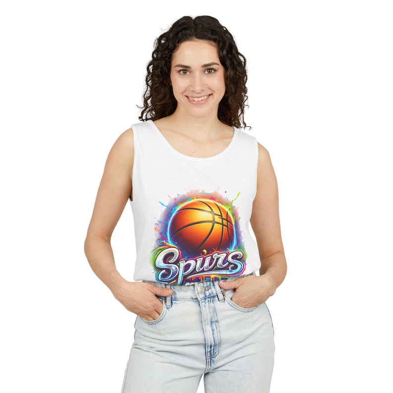May include: White tank top featuring a basketball graphic with the word "Spurs" in a colorful design. The basketball is orange with black lines, set against a vibrant, multi-colored splash.