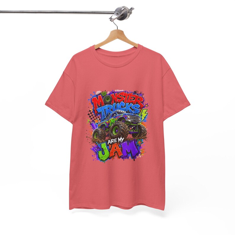 Może przedstawiać: Koralowa koszulka z kolorową grafiką monster trucka. Grafika zawiera napis "MONSTER TRUCKS ARE MY JAM" w stylu graffiti z żywymi kolorami, takimi jak niebieski, zielony i fioletowy.