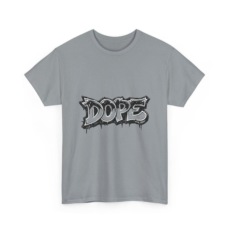 May include: A light gray t-shirt featuring the word "DOPE" in a graffiti-style design. The word is rendered in black and white with dripping paint effects, creating a bold and urban aesthetic. The shirt is a classic crew neck style.