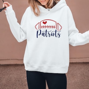May include: White hoodie with a red and blue football graphic and the word "Patriots" in a script font. The graphic includes a red heart. The hoodie has long sleeves and a hood.