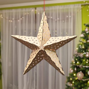 May include: A large, five-pointed star-shaped decoration made of light-colored wood. The star has numerous small, star-shaped cutouts throughout its surface. It is suspended from a red string, suggesting it is a hanging ornament, possibly for the holidays.