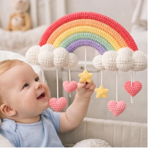 May include: A colorful crochet baby mobile featuring a rainbow, white clouds, pink hearts, and yellow stars. The rainbow arches in red, orange, yellow, green, blue, and purple. The mobile is designed for a nursery.