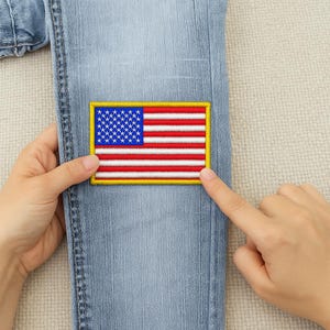 Peut inclure: Écusson brodé du drapeau américain avec une bordure jaune, des rayures rouges et blanches et un champ bleu d'étoiles blanches. L'écusson est présenté sur un jean bleu clair.