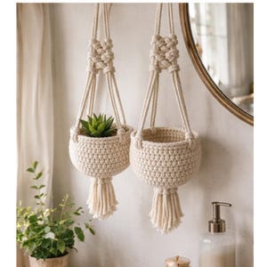 Peut inclure: Deux suspensions macramé blanc cassé, chacune avec un panier tissé et une frange. L'une contient une plante succulente verte. Les suspensions sont suspendues à un sommet noué, conçu pour la décoration intérieure. Le style est bohème et naturel.