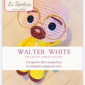 以下が含まれることがあります： 手作りの編みぐるみ人形、ウォルター・ホワイト。 禿げ頭、丸いメガネ、茶色の口ひげが特徴です。 黄色のジャケットを着ています。 テキスト「WALTER WHITE」が下に表示されています。