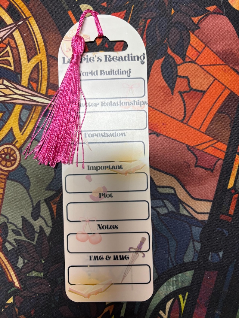 K&ouml;nnte beinhalten: Ein wei&szlig;es Lesezeichen mit einem rosa Quasten. Das Lesezeichen hat den Text "La Pie's Reading World Building" und Abschnitte f&uuml;r "Character Relationships", "Foreshadow", "Important", "Plot", "Notes" und "FMC & MMC".