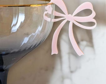 Peut inclure: Un nœud en plastique rose en forme de ruban, conçu pour être attaché à un pied de verre. Le nœud est attaché à une flûte à champagne.