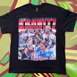 May include: A black short-sleeve t-shirt featuring a graphic print of Ted Kravitz. The design includes multiple photographs of the reporter with microphones and headsets, the text "TED KRAVITZ" in large red and white letters, and "Two Secs Ted".