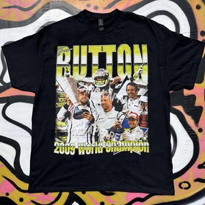 May include: Black t-shirt featuring a graphic of a race car driver with the word "BUTTON" in large yellow letters. The graphic includes the text "2009 World Champion".