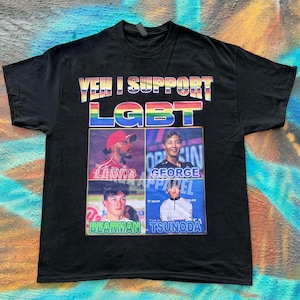 May include: A black short-sleeve t-shirt featuring the text YEH I SUPPORT LGBT in rainbow colors. Below the text are four photographic portraits of race car drivers labeled Lewis, George, Bearman, and Tsunoda, arranged in a grid format.