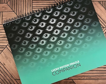 Puede incluir: Una libreta de espiral verde y negra con un patrón repetitivo de ojos. La libreta tiene el texto "Lucky Potion Oracle Companion" impreso en la portada.