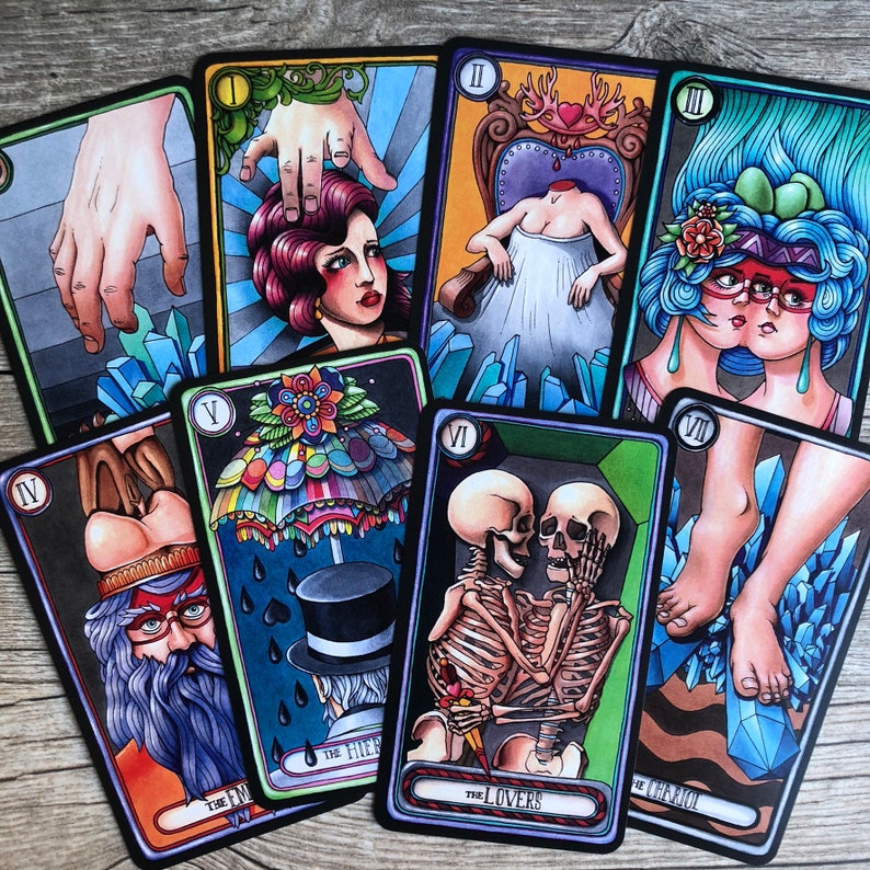 May include: Tarot card deck with colorful illustrations. The cards feature a variety of imagery, including skeletons, hands, and a woman with a crown. The cards are numbered with Roman numerals and have titles such as "The Lovers" and "The Emperor".