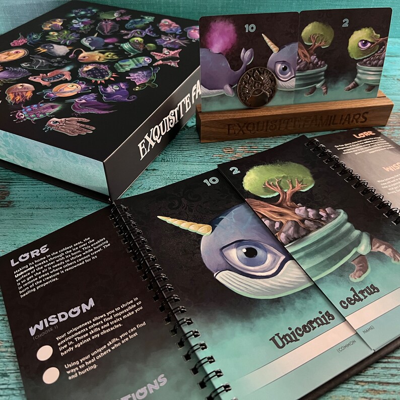 Puede incluir: Un juego de cartas llamado "Exquisite Familiars". Las cartas presentan ilustraciones de criaturas fant&aacute;sticas, incluyendo un unicornio con cuerpo azul y un gran ojo, y un &aacute;rbol que crece en una maceta. Las cartas est&aacute;n numeradas 10 y 2. El libro de reglas del juego est&aacute; abierto en una p&aacute;gina con el t&iacute;tulo "Lore" y una descripci&oacute;n de la criatura unicornio.