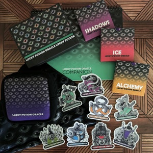 May include: A set of Lucky Potion Oracle cards and companion guidebook with a black and green eye pattern. The set includes cards for Shadows, Ice, and Alchemy. There are also several stickers with different designs, including a snake, a skull, and a mushroom.