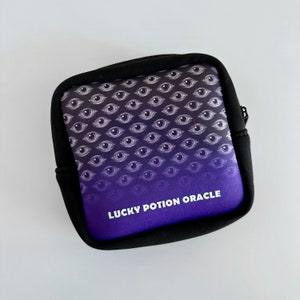 May include: A purple and black zippered pouch with a repeating eye pattern and the text "LUCKY POTION ORACLE" printed on the front.