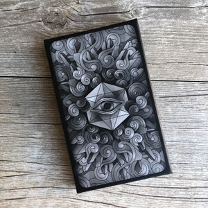 May include: Black and white illustration of a geometric eye with a detailed background of swirling clouds and crystals. The eye is surrounded by a geometric shape with a white outline.