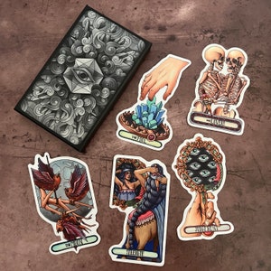 May include: A set of ten tarot cards with colorful illustrations and gold accents. The cards feature images of The Fool, The Lovers, The Moon, Strength, and Judgement. Each card has a title printed on it.