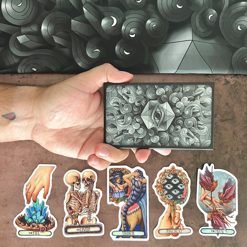 May include: A set of ten tarot cards with colorful illustrations and gold accents. The cards feature themes such as The Fool, The Lovers, Strength, The Chariot, and The Moon. Each card has a title and a corresponding image.