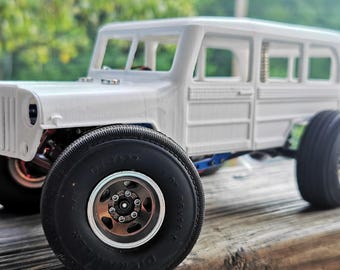 Op de afbeelding: Een wit model van een SUV in vintage-stijl met grote zwarte banden en bronskleurige velgen. Het voertuig heeft een gedetailleerde grille, ramen en een houten paneel aan de zijkanten. Het model staat op een houten oppervlak.