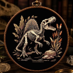 May include: A circular wooden embroidery hoop containing a cross-stitch pattern of a Spinosaurus skeleton on a black fabric background. The dinosaur is depicted in profile with its mouth open, surrounded by stitched foliage and a rock formation.