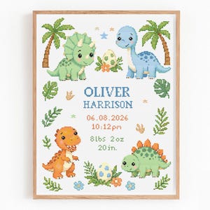 May include: A framed cross-stitch pattern featuring four colorful cartoon dinosaurs, palm trees, and foliage. The text reads OLIVER HARRISON, 06.08.2026, 10:12pm, 8lbs 2oz, and 20in. The design includes two speckled dinosaur eggs and small stars.