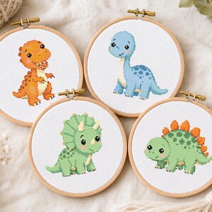 Può includere: Quattro telai da ricamo circolari in legno contenenti motivi a punto croce di dinosauri. I disegni raffigurano un T-Rex arancione, un dinosauro blu dal collo lungo, un triceratopo verde e uno stegosauro verde con placche arancioni.