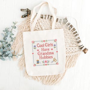 Looking for a funny cross stitch pattern for a craft lover? This Cool Girls Have Grandma Hobbies PDF pattern is a charming choice for stitchers, makers, and creative friends. The design features a readable quote in classic cross stitch lettering, surrounded by traditional flowers, hearts, craft tools, and a simple border. It has a cozy vintage feel that makes it perfect for framed wall art, handmade decor, or a unique gift for someone who loves grandma hobbies.