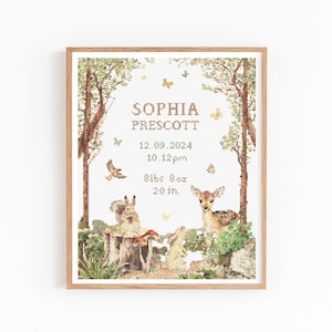 Op de afbeelding: Een ingelijste kruissteek geboorteaankondiging met een boslandschap met een hert, eekhoorn en konijn. De tekst luidt "SOPHIA PRESCOTT" met geboortegegevens: 3,9 kg, 50,8 cm, en de geboortedatum en -tijd.
