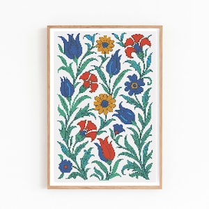 May include: A framed floral cross-stitch pattern featuring a symmetrical design of blue, red, and yellow flowers with green leaves on a white background. The artwork is displayed in a light brown wooden frame.