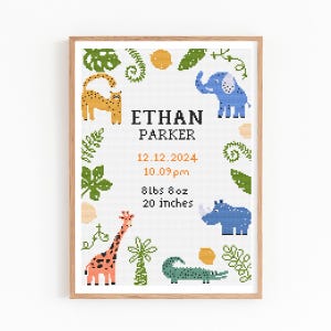 May include: A framed cross-stitch birth announcement with a giraffe, elephant, and other animals. The announcement includes the name "ETHAN PARKER", date, time, weight (3.9 kg), and height (50.8 cm). The frame is a light brown colour.